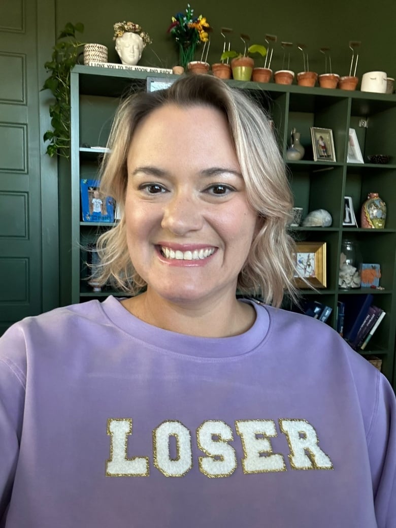 Selfie of smiling blonde woman in a purple sweatshirt that reads "LOSER" in big white letters