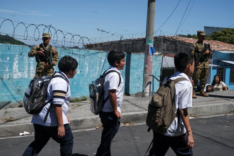 Schoolchildren walk past soldiers in the street.