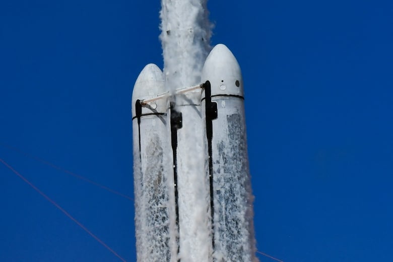 A big rocket covered in ice is taking off mid-air against a blue sky backdrop.