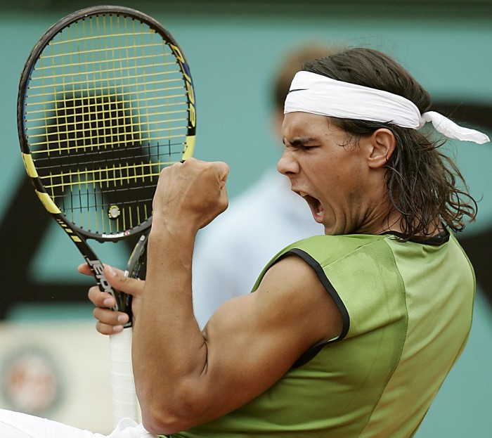 Rafael Nadal celebrates with a fist pump after winning a point. He is wearing a green sleeveless shirt and a white headband.