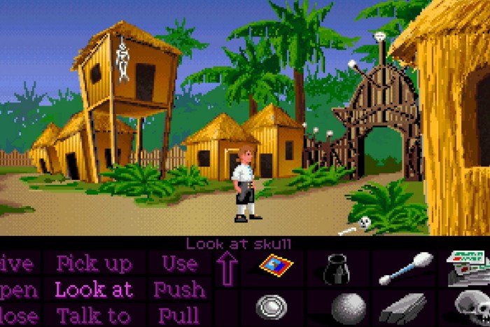 An image from a video game shows a character standing in a village of simple dwellings in a tropical setting, with a toolbar at the bottom of the screen