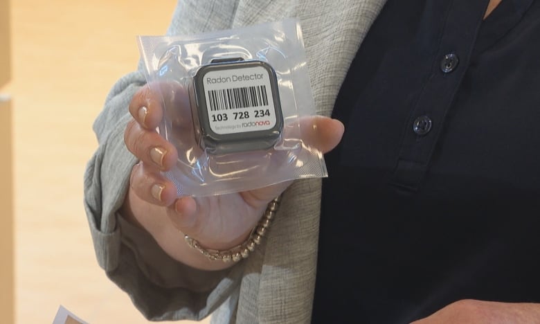 A woman holding a small square plastic device with a barcode on it, wrapped in plastic