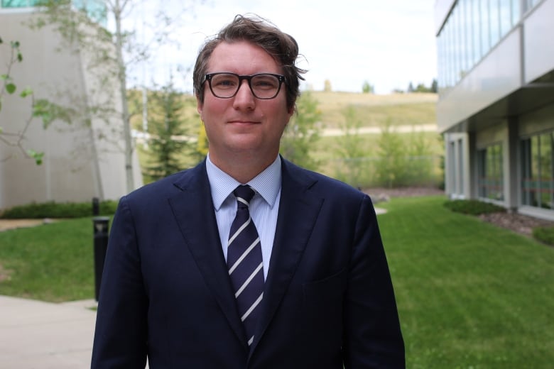 A man wearing a suit and glasses stands outside an office building in Calgary, Alta.