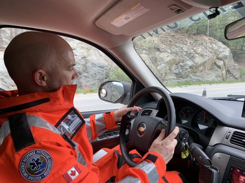 A man in an orange jumper sits in a vehicle.