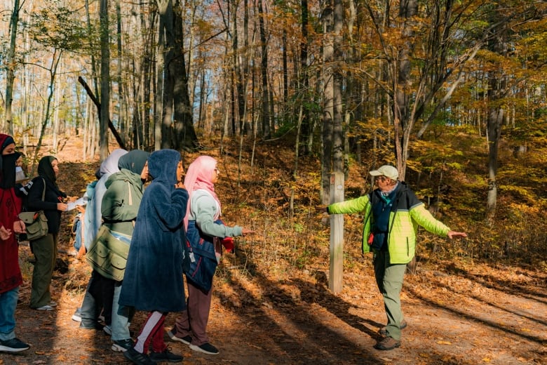 A group of students and one guide walk along a path through a deciduous forest.