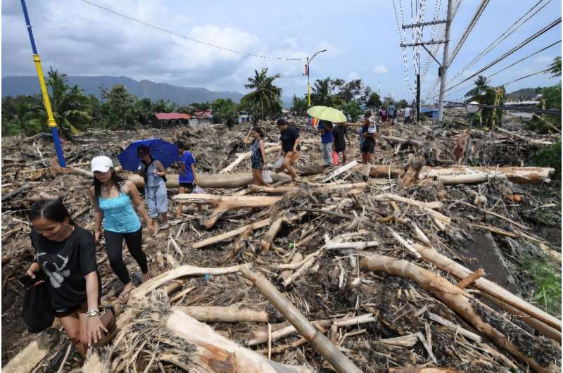 People walk through logs swept away by Tropical Storm Trami in Laurel, Batangas province, south of Manila