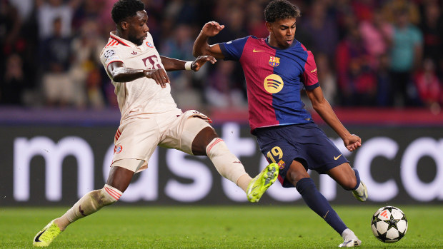 Lamine Yamal of Barcelona shoots under pressure from Alphonso Davies of Bayern Munich.