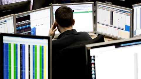 A trader surrounded by multiple computer monitors, displaying financial data