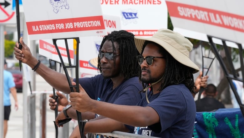 Two men stand side by side, holding signs that say "ILA Stands for Job Protection". 