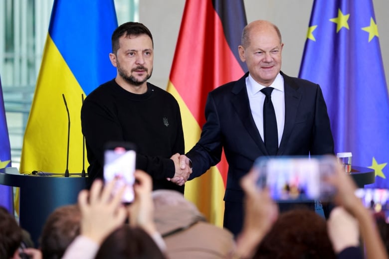 Two men shake hands in front of Ukrainian, German and EU flags.