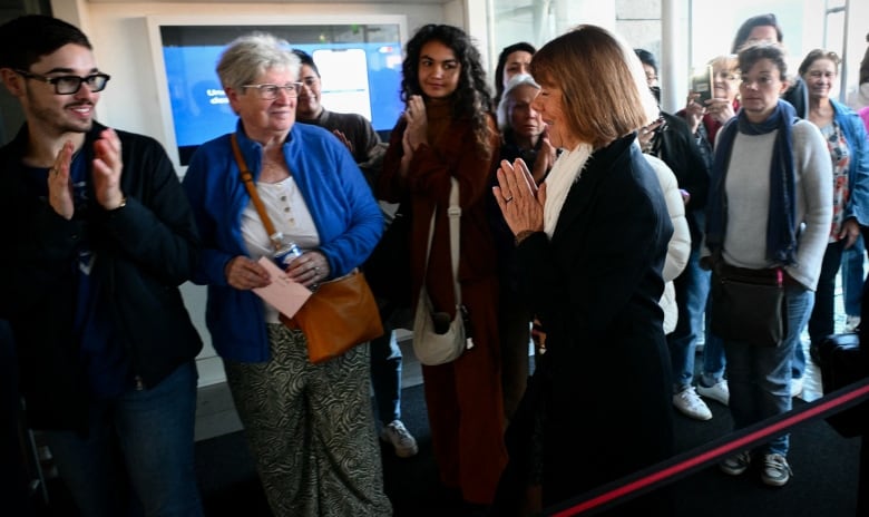 A woman clasps her hands together while walking past supporters in  a court house