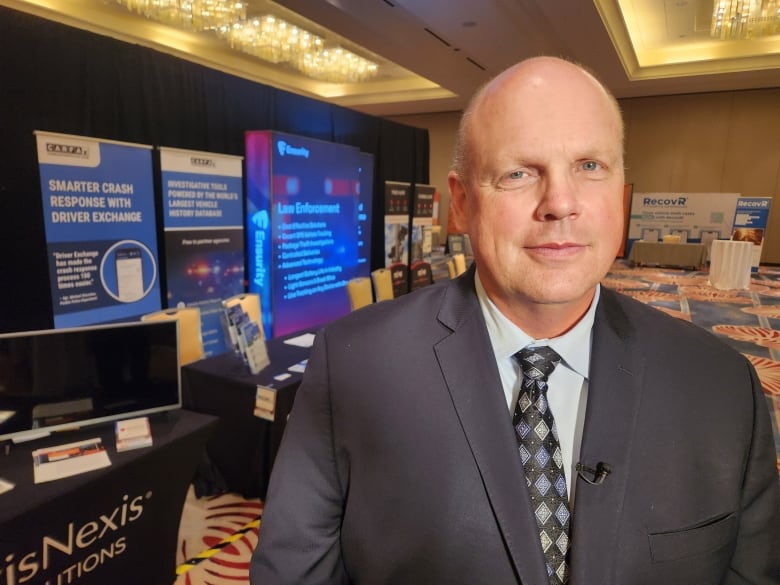 A man looks at the camera, with conference booths set up behind him.