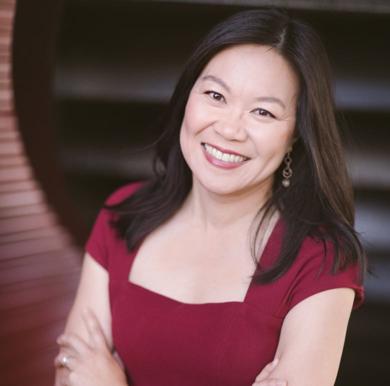 A woman in a burgundy dress poses for a portrait with arms crossed.