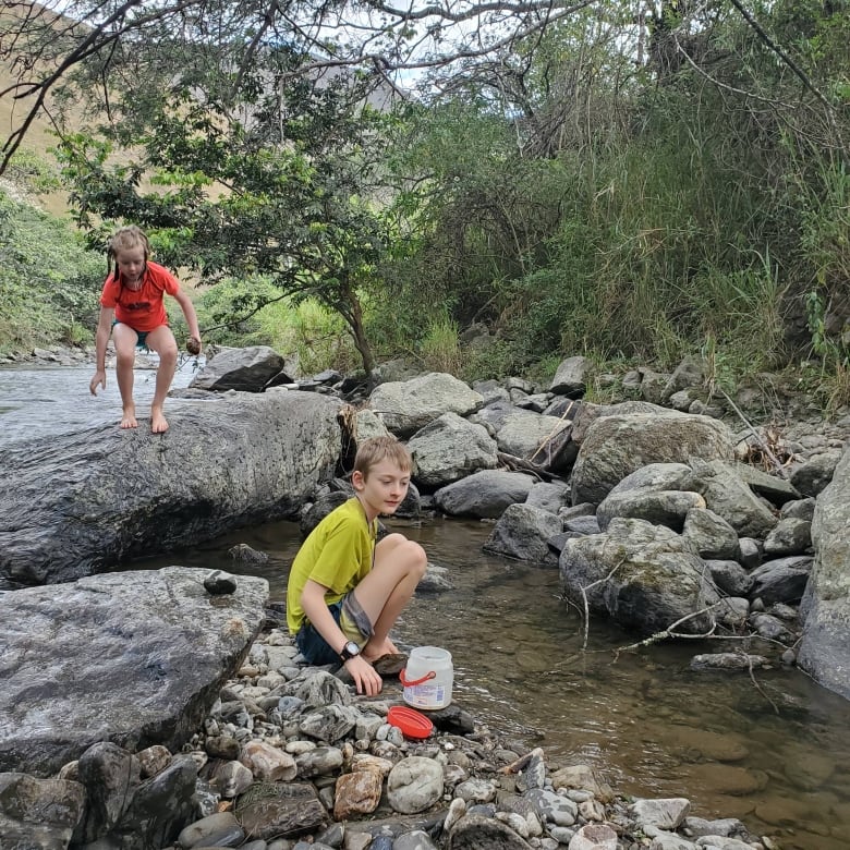 Two children are seen on the rocks next to a river.