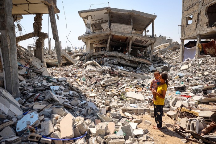 A woman stands holding a child surrounded by the rubble of buildings destroyed during an Israeli bombardment in Khan Younis in the southern Gaza Strip