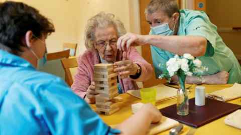 Elderly woman plays Jenga with care workers