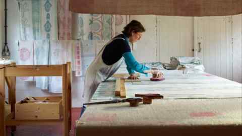 Image depicts a woman engaged in a textile printing or crafting activity in a well-organised studio