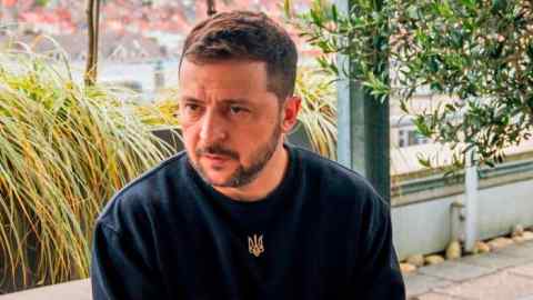 Volodymyr Zelenskyy is seated outdoors, wearing a black shirt with a Ukrainian trident emblem during an interview with the FT