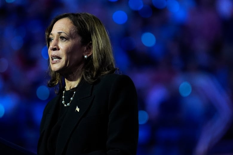 A woman with shoulder-length brunette hair is seen on stage at a political rally wearing a black suit.