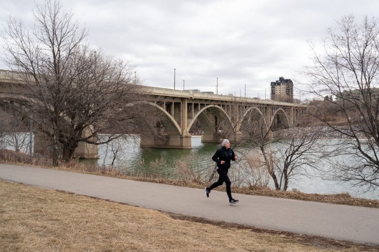 A person runs on a sidewalk alongside a bridge