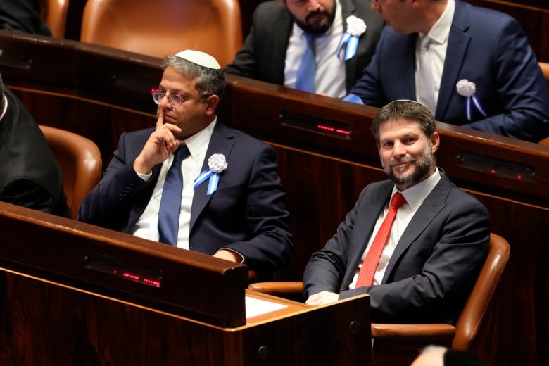 Two men in suits sitting at a government board table.