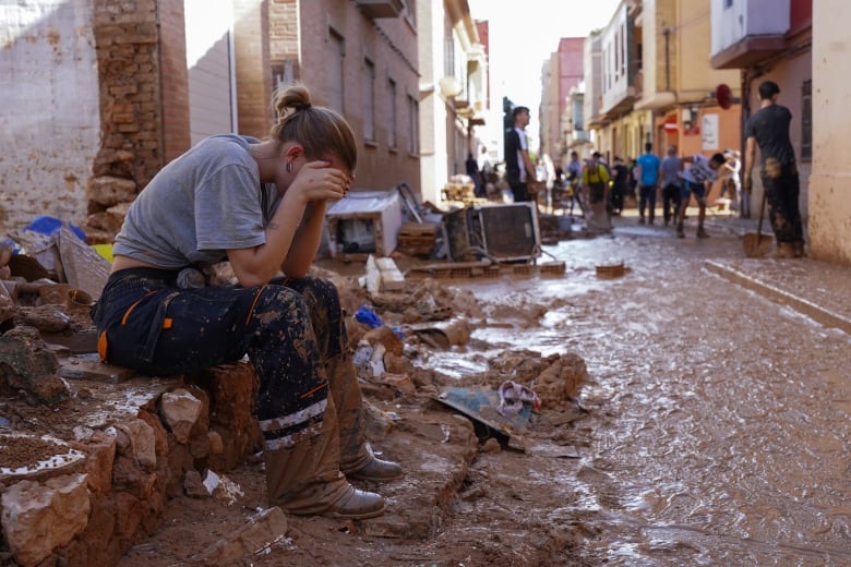 A woman rests her forehead in her hands on a curb.