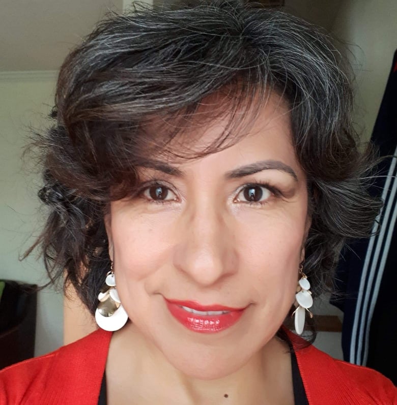 A close-up of a woman with white earrings and a red top.