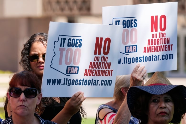 People hold up signs with the slogan 'it goes too far' printed in red and blue ink.