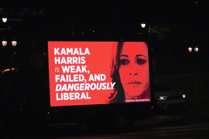 A night-time shot of a billboard illuminated in red against the dark, with the words ‘Kamala Harris is weak, failed and dangerously liberal’