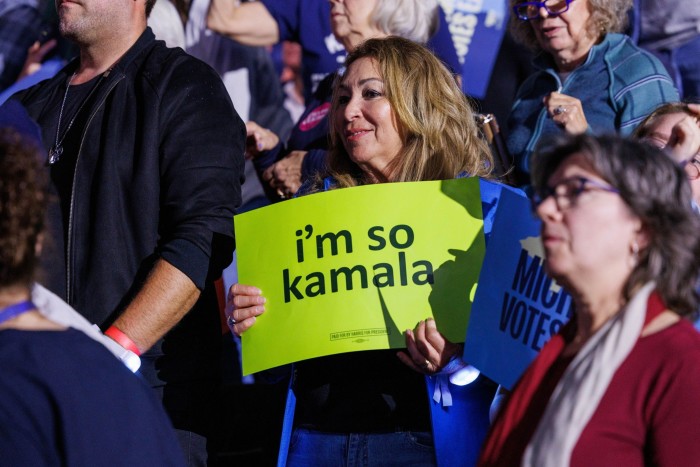 A crowd of people, many of them wearing blue, some holding blue placards with the words ‘Michigan votes’. At the centre is a woman holding a lime-green placard with the words ‘I’m so Kamala’ in lower-case letters