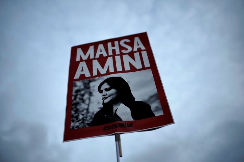 A woman holds a red placard with a picture of an Iranian woman during a protest against her death.