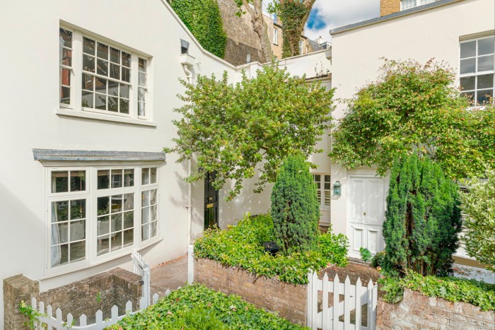 A white rendered cottage in a corner, at right angles to the neighbouring house. It has a bow window on the ground floor and a white wooden gate to a very small front garden area