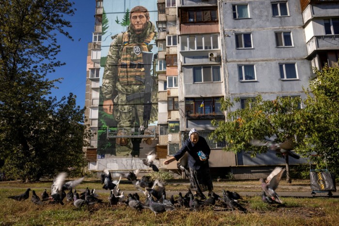 A woman feeds pigeons in front of a mural by Ukrainian street artist Eugene Gladenko showing the fallen Ukrainian soldier Maksym Bordus, amid Russia’s attack on Ukraine, in Kyiv