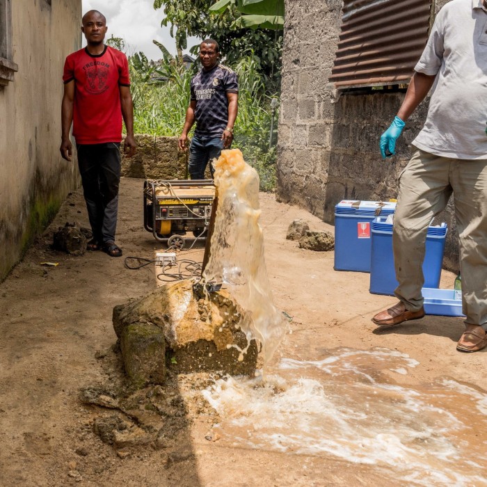 People carry buckets of water as water gushes from a well