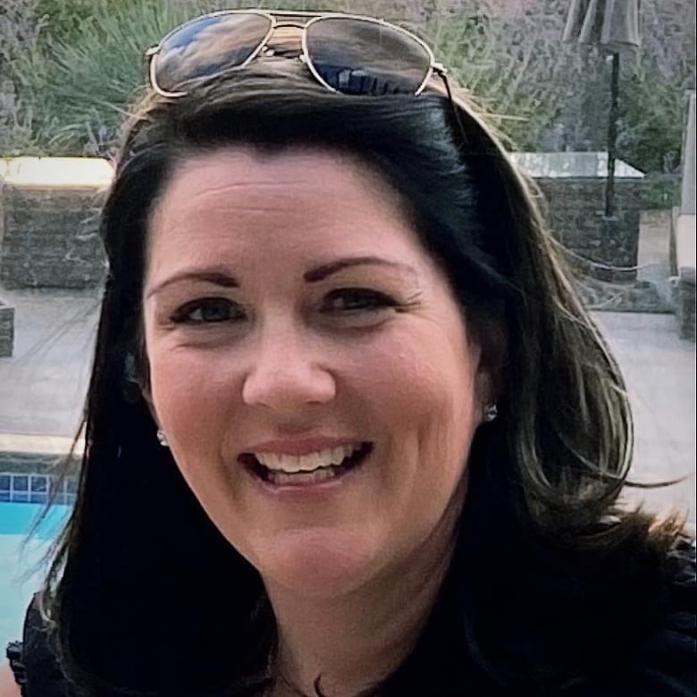 A woman with sunglasses over her head smiles in front of a pool.