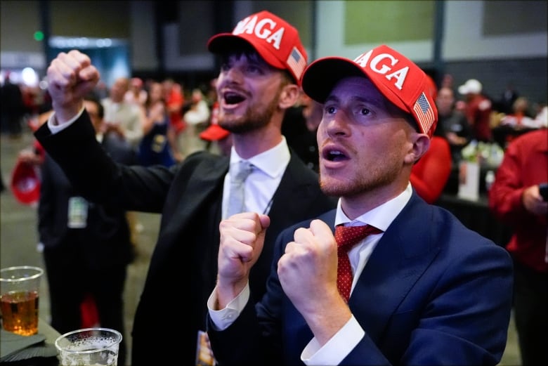 Two men in red baseball caps with "MAGA" written in white letters raise their fists.