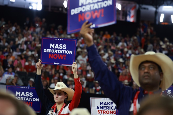 People wearing cowboy hats stand in a crowd holding up signs that read ‘mass deportation now’