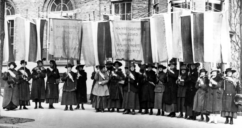 Suffragettes march with signs.