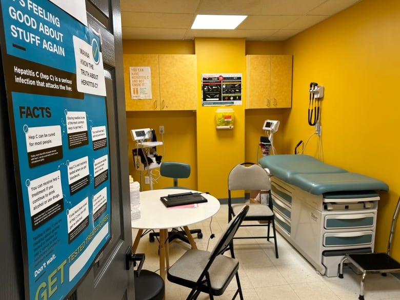 A look through the door to a medical room with bright yellow walls, a table and chairs, a table to lay on and other medical equipment. 