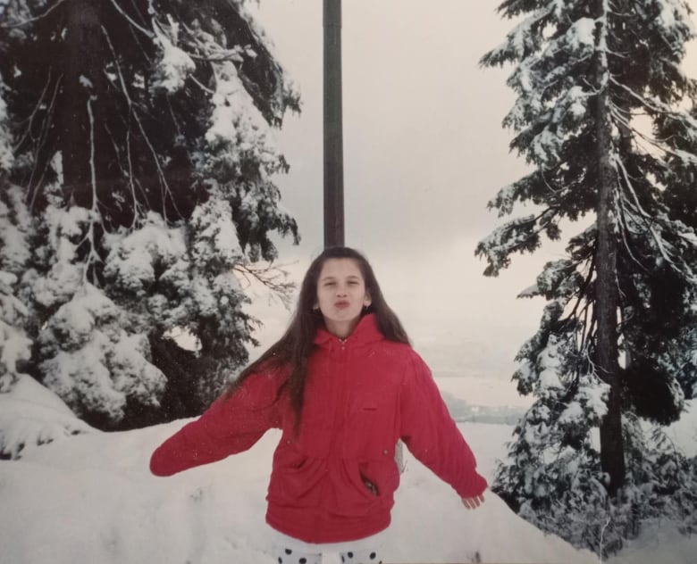 A girl in a red winter jacket stands outside in snow. 