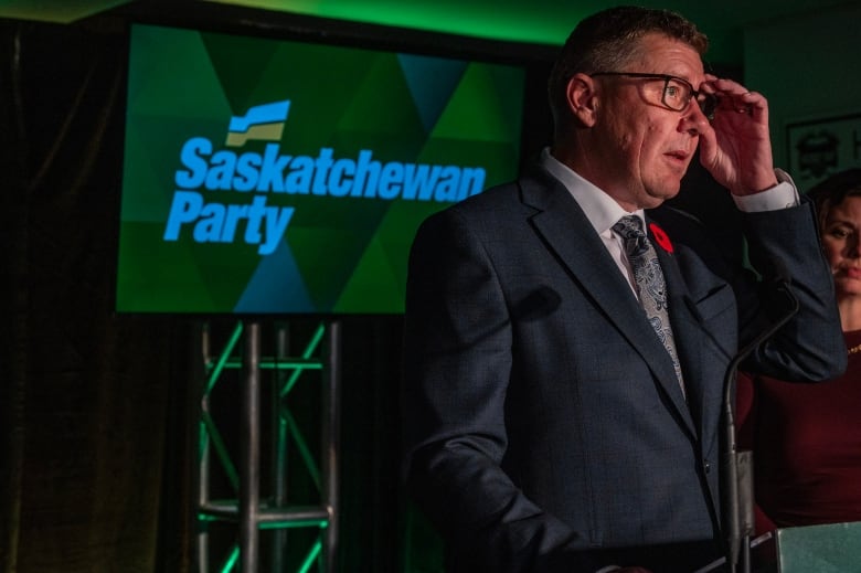 a man in a suit and tie fixes his glasses at a podium