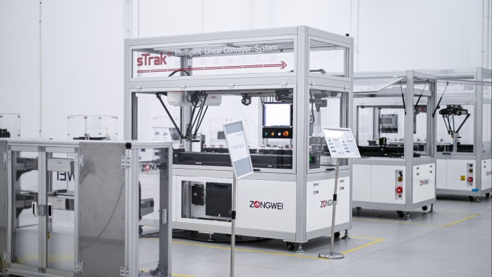 Industrial machines with clear enclosures labeled ‘Zongwei’ are set up in a clean, white workspace, with one machine featuring robotic arms for handling objects