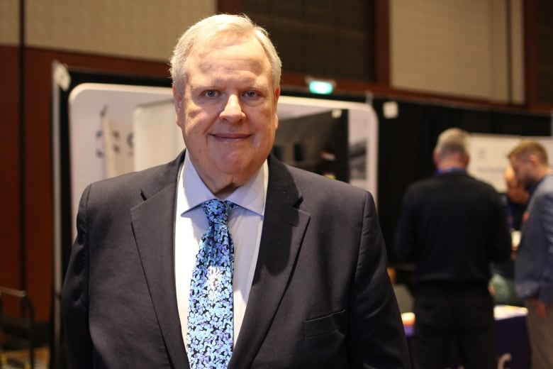 A man in a navy suit and blue patterned tie is pictured in a Hyatt Regency ballroom.