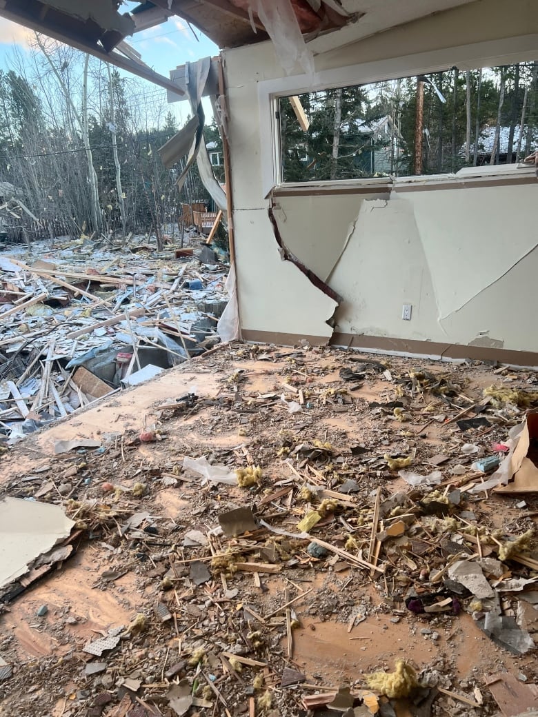 A room missing a wall with debris covering the floor and damage to the other wall and roof.