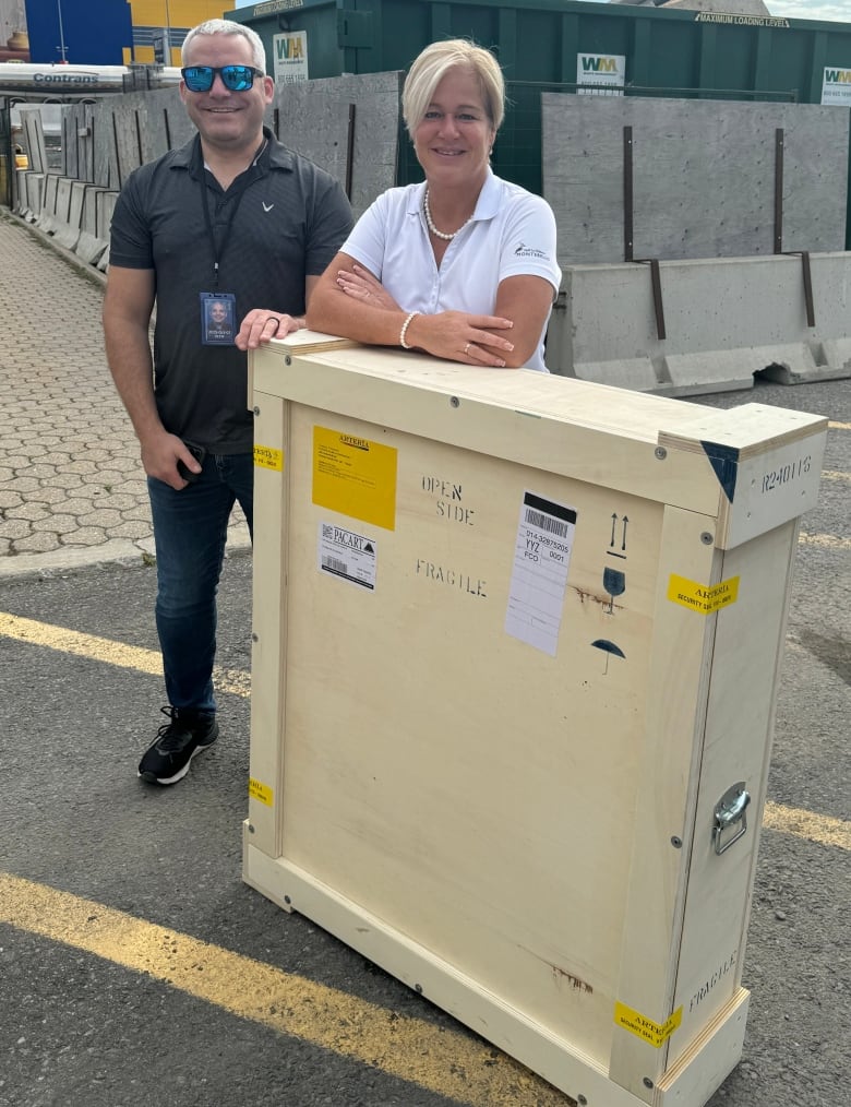 Two people stand with a large wooden box.