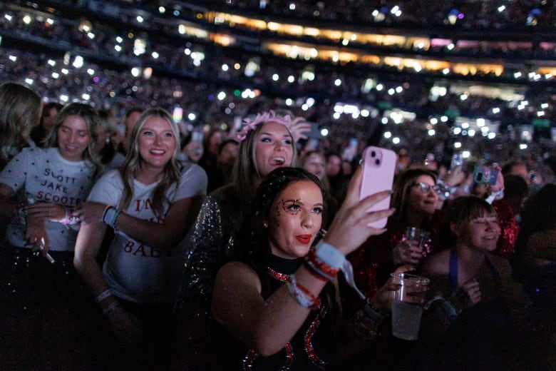 Fans wearing Taylor Swift outfits hold their phones up as they watch the stage. 