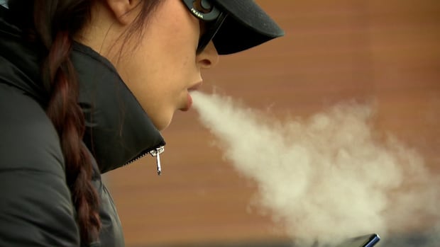 A woman blows vape smoke into the air