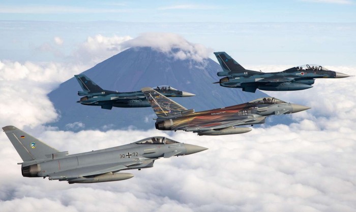 Four fighter jets, including Eurofighters, fly in formation over clouds with Mount Fuji in the background