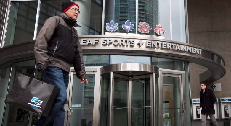 A man walks in front of the curved outside of the building. 