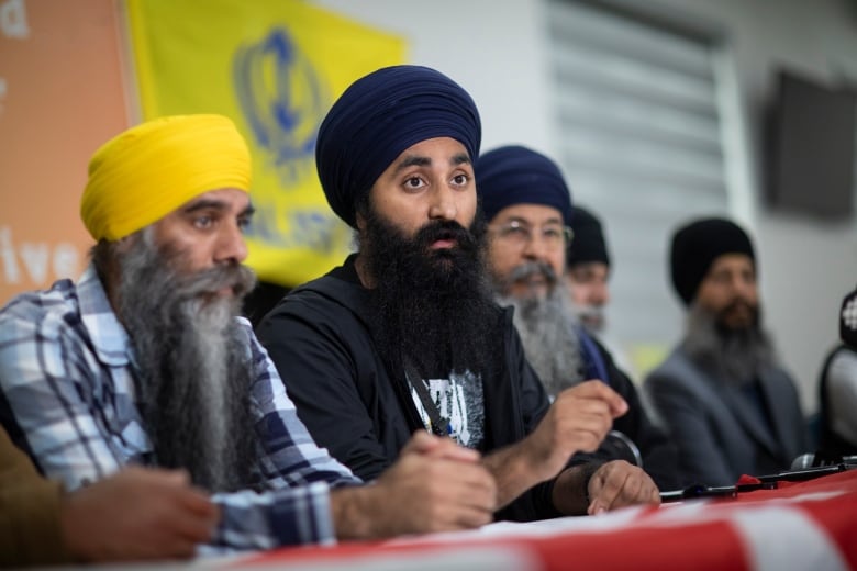 A row of Sikh men sit at a table, with the one in the centre speaking.